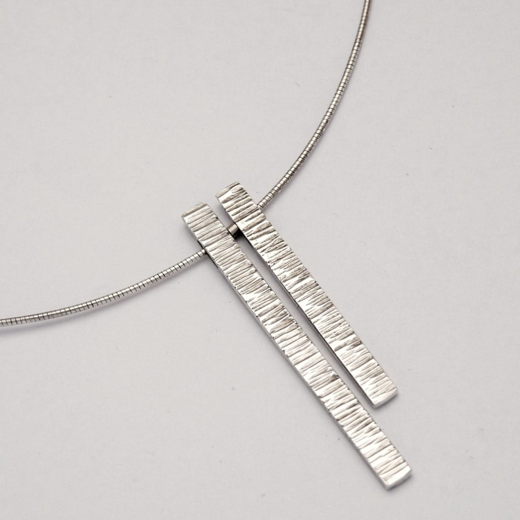 Close image of the two different length hammer textured lengths from the from, hanging from the curve of omega necklet